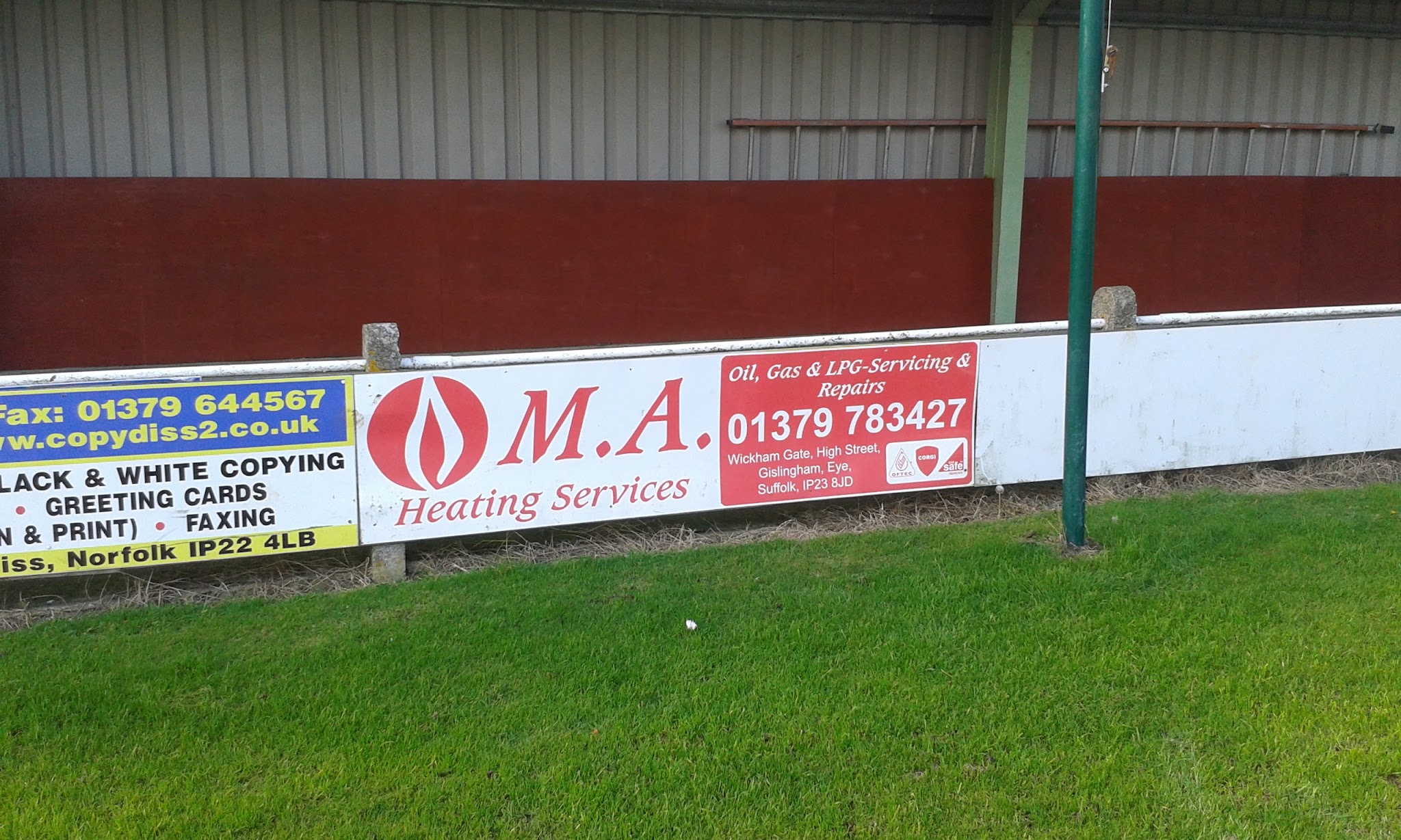 An MA Heating Services banner with the phone number 01379 783427 on a sports ground fence